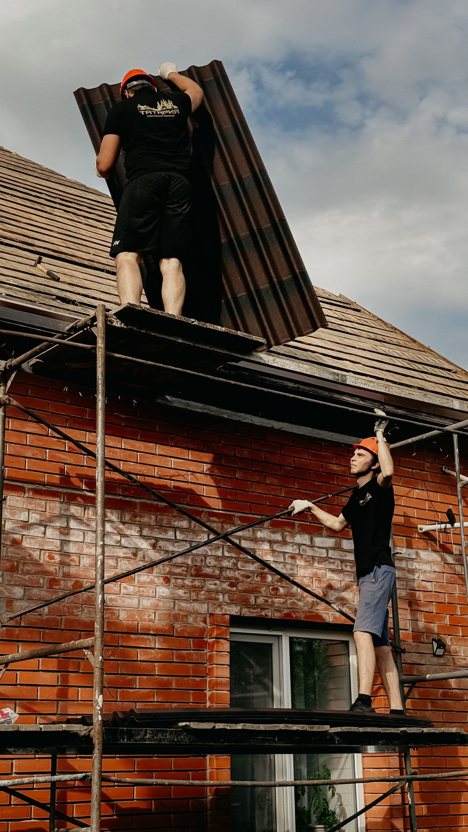 Roofers on scaffolding installing roof sheets on a house