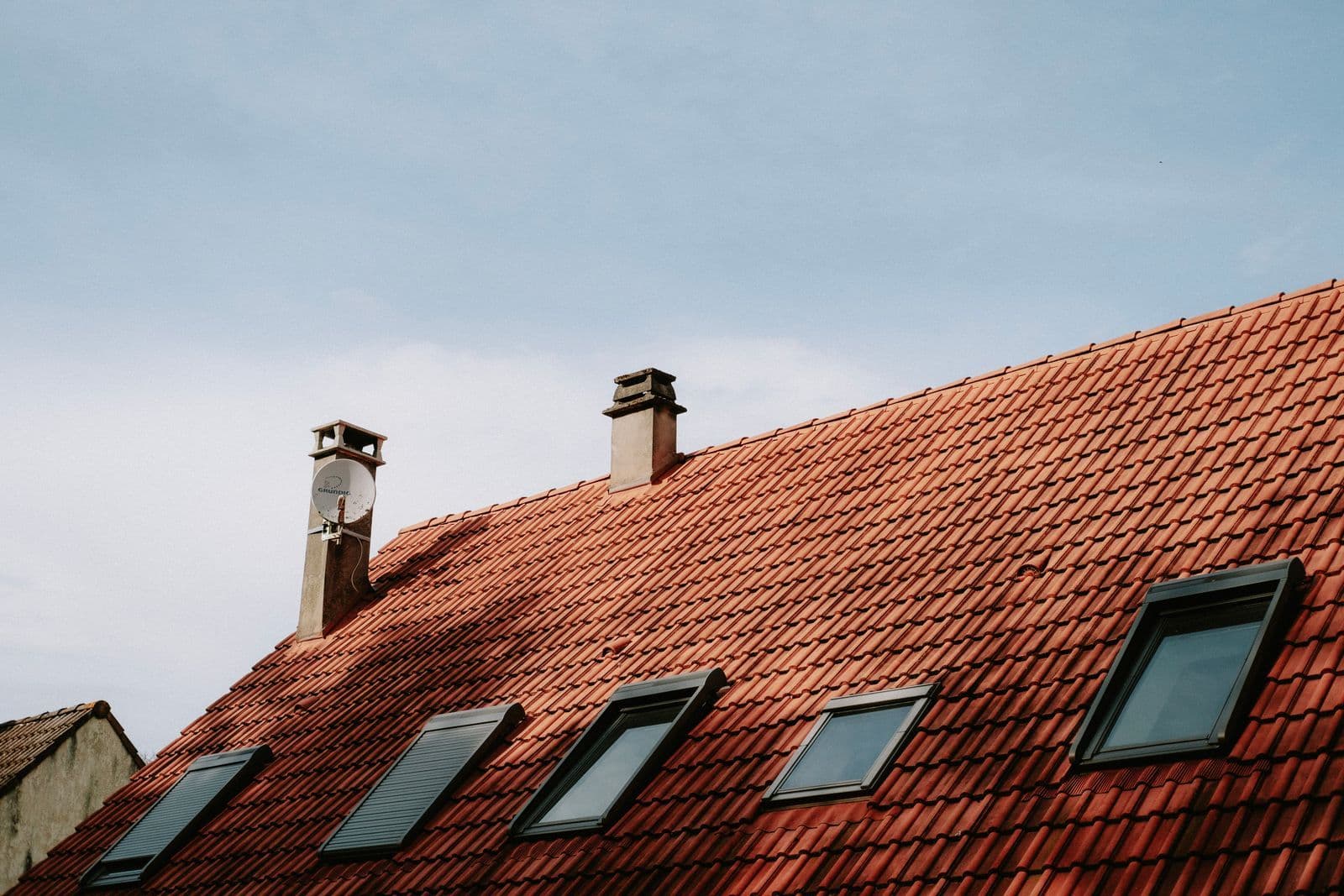 Clay-tiled house roof with chimneys and roof windows against a blue sky